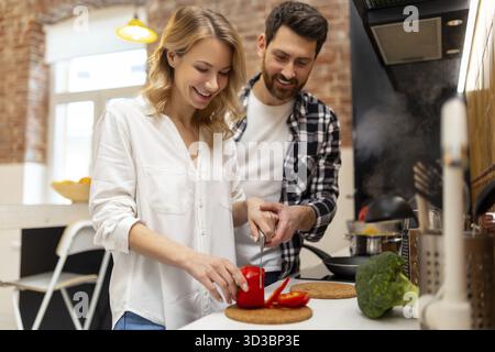 Amata giovane coppia che taglia verdure al bancone del cucinino, uomo e donna innamorati cucinare cibo insieme a casa Foto Stock