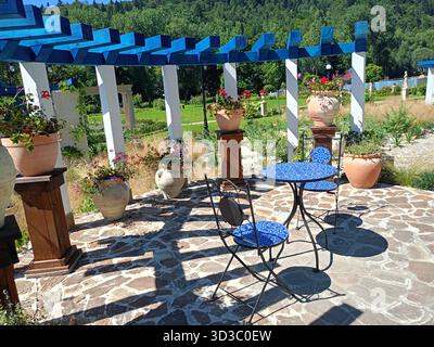 Muszyna, Voivodato di Malopolska, Polonia - 12 agosto 2025 - patio decorativo con un tavolo a mosaico blu e sedie in ferro battuto sotto un legno Foto Stock