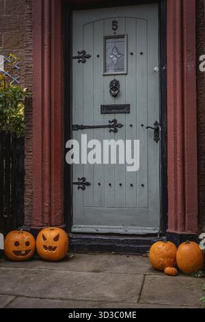 Festa autunnale di zucche decorative di Halloween in varie dimensioni e colori, sparse artisticamente sul terreno prima dell'ingresso di una casa Foto Stock