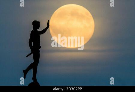 Hannover, Germania. 5 novembre 2025. La luna sorge all'orizzonte dietro la statua del "Torchbearer" (1937) sulla riva settentrionale del Maschsee. La sera, la più grande luna piena dell'anno può essere vista sulla Germania - una cosiddetta superluna. Credito: Julian Stratenschulte/dpa/Alamy Live News Foto Stock