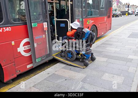 Giovani disabili seduti su una rampa di imbarco per scooter motorizzati per la mobilità in sedia a rotelle per accedere all'autobus cittadino dal marciapiede a Londra Regno Unito KATHY DEWITT Foto Stock
