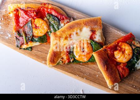 Pizza mediterranea preparata al momento con gamberetti su una tavola di legno e un tavolo bianco. Foto di alta qualità Foto Stock