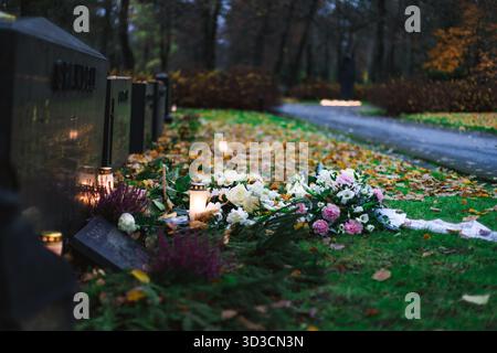 Candele accese su un cimitero di notte, calde fiamme che creano un'atmosfera commemorativa calma ed emotiva tra le tombe. Foto Stock