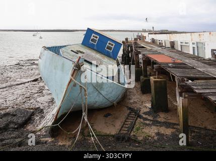 Barca spiaggiata dalla bassa marea vicino ad un vecchio molo di legno, Burnham a Crouch, Essex, Inghilterra. Foto Stock