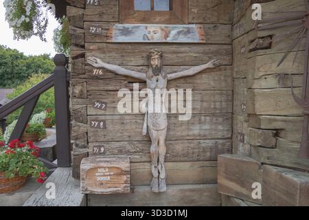 Crocifisso in legno di Gesù montato su un muro rustico di tronchi con fiori nelle vicinanze di Chisinau, Moldavia - 15 settembre 2025 Foto Stock