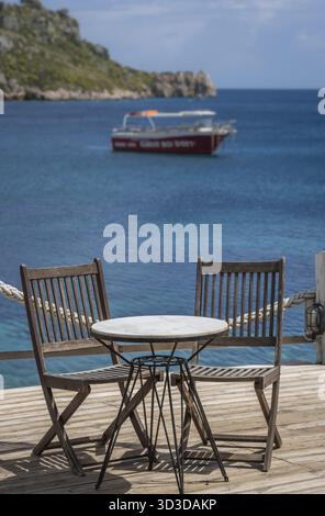 Sedie di legno dai vuoti di un ristorante esterno tavola su una piattaforma di coperta in Agios Nikolaos beach sull'isola di Zante, Grecia Foto Stock