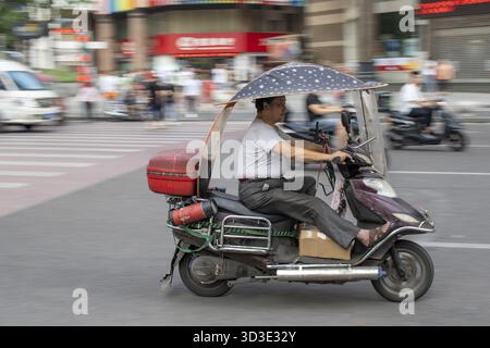 Chongqing, Cina - Agosto 2019 : uomo che guida pericolosamente veloce in uno scooter sulla strada congestionata Foto Stock