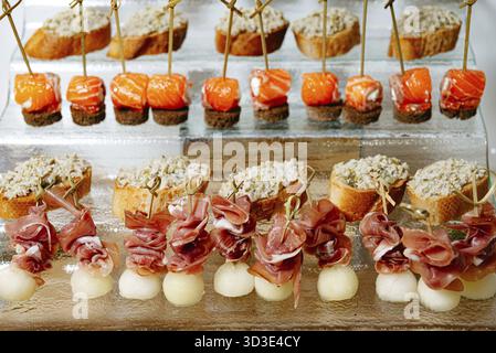 Cibo, Una lussuosa gamma di tartine con salmone affumicato, melone avvolto al prosciutto e formaggio su pane croccante, splendidamente disposto su un bicchiere di vino Foto Stock