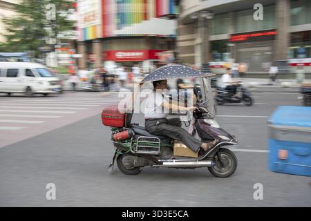 Chongqing, Cina - Agosto 2019 : uomo che guida pericolosamente veloce in uno scooter sulla strada congestionata Foto Stock