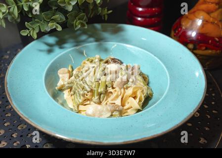 Cibo, deliziose tagliatelle cremose condite con asparagi verdi saltati e funghi serviti in un vivace piatto turchese Foto Stock