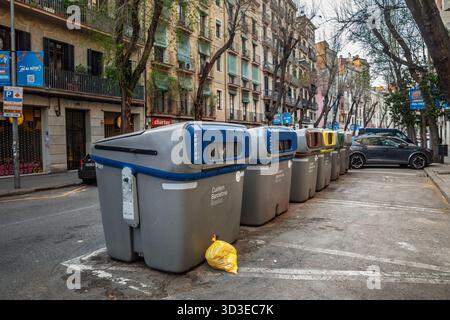 BARCELLONA, SPAGNA - 5 APRILE 2025: Fila di contenitori per riciclaggio grigi con codice colore su una strada di Barcellona contrassegnata. gli scomparti mostrano la raccolta selettiva per la carta Foto Stock