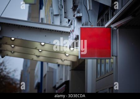 Un'insegna quadrata rossa vuota della scatola luminosa pende da una facciata commerciale su una strada della città del Nord America, sotto tende metalliche e piccole lampade. pannello vuoto pr Foto Stock