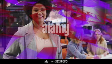 Donna in piedi che indossa un blazer grigio e sorride in un ufficio di coworking con notebook e tazze da caffè Foto Stock