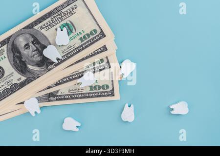 Modelli in legno di denti su banconote da un dollaro su sfondo blu isolato, il concetto di assicurazione, trattamento dentale a pagamento e implantologia. Foto Stock