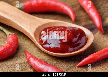 Cucchiaio di legno di pasta di peperoncino piccante tra peperoncini freschi Foto Stock