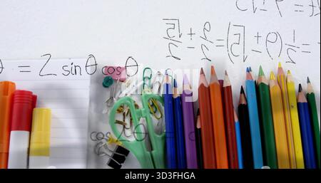 Visualizzazione di cancelleria sulla scrivania dello studio con matite colorate, forbici, clip, spille e scarabocchi matematici Foto Stock