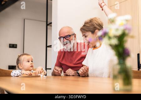 Scena calda di nonni che trascorrono del tempo di qualità con la nipote a tavola. Le interazioni gioiose evidenziano il legame familiare e l'happy Foto Stock