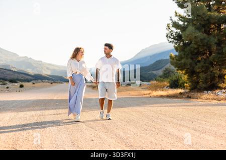 Una coppia gode di una tranquilla passeggiata mano nella mano lungo una strada sterrata illuminata dal sole in Turchia. Circondati da una tranquilla bellezza naturale, condividono un momento di tranqui Foto Stock