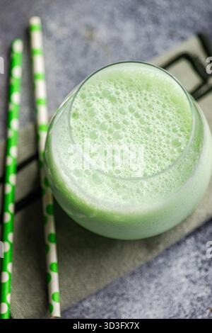 Latte matcha cremoso in un bicchiere con schiuma, accompagnato da due paillette verdi a pois su una superficie ruvida. Una bevanda rinfrescante perfetta per il tè lo Foto Stock