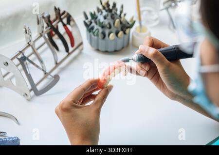 Dall'alto odontoiatrica femminile irriconoscibile che lavora minuziosamente su una protesi dentale utilizzando uno strumento, dimostrando la maestria artigianale e la tecnica Foto Stock