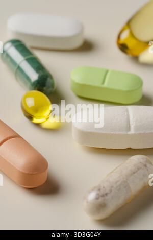 Un assortimento di pillole colorate e integratori, tra cui capsule verdi, bianche, gialle e marroni, sono disposti su sfondo beige, evidenziando di Foto Stock