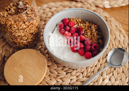 Una deliziosa ciotola di muesli fatti in casa condita con bacche rosse fresche, perfettamente sistemata su un tappeto rustico. I colori vivaci e le texture creano un Foto Stock