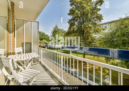 Un ampio balcone con sedie bianche che si affacciano su una vegetazione lussureggiante e un cielo azzurro, perfetto per rilassarsi e godersi la natura Foto Stock