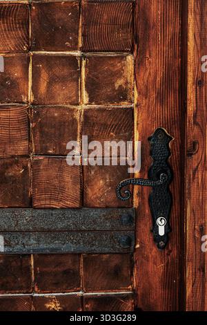 Un primo piano di una porta rustica in legno che mostra texture intricate e patina invecchiata. Il manico in metallo aggiunge un tocco vintage, mettendo in risalto la maestria artigianale e. Foto Stock