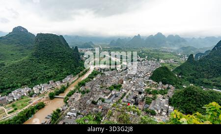 Vista panoramica dell'antica città di Xingping dalla cima del colle Laozhai, con lussureggianti montagne verdi e un fiume tortuoso che attraversa il pittoresco paesaggio Foto Stock