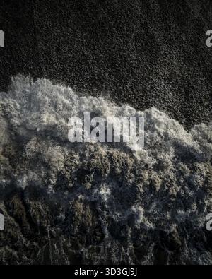 Vista aerea delle onde tumultuose che si infrangono contro le scure sabbie vulcaniche della spiaggia, creando un netto contrasto tra luce e ombra, Bali, Indon Foto Stock