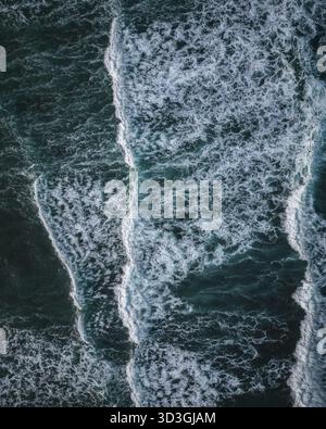 Vista aerea dell'affascinante oceano turchese, dove le onde bianche schiantano contro la costa scura e frastagliata, creando un contrasto incredibile, Bali, Foto Stock