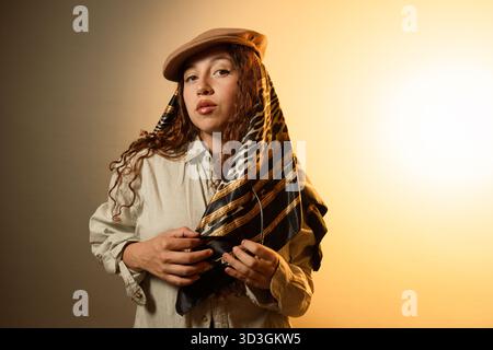 Giovane donna che indossa una sciarpa alla moda con un cappello newsboy in una calda luce da studio Foto Stock