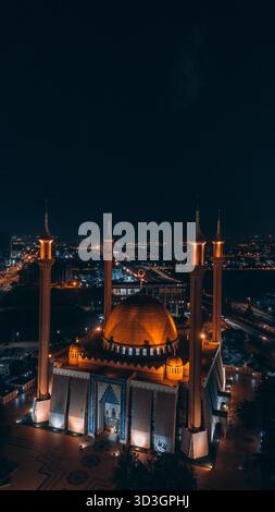 Veduta aerea di una moschea a cupola dorata illuminata contro il cielo notturno buio, i suoi minareti che brillano come fari, Abuja, territorio della capitale federale, Nige Foto Stock