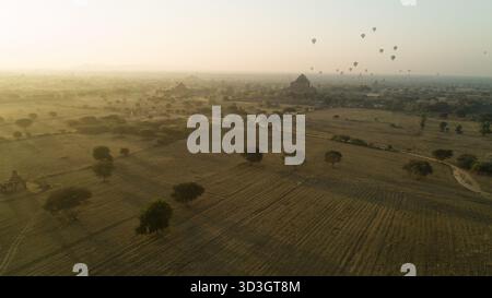 Vista aerea delle mongolfiere che si spostano serenamente sopra gli antichi templi e le pianure dorate, gettando lunghe ombre nella luce soffusa del mattino, il vecchio Bagan, Foto Stock