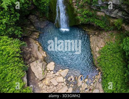 Vista aerea della cascata che si getta in una piscina turchese circondata da alberi verdeggianti e affioramenti rocciosi, Shirābād, Ramian, Iran. Foto Stock