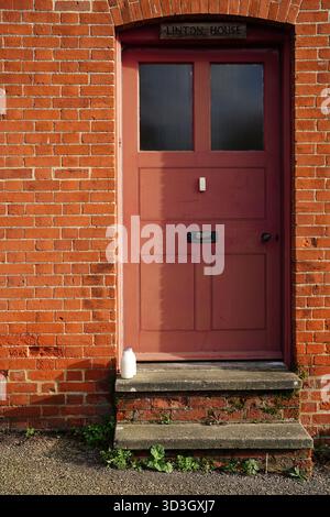 Una porta rossa di un edificio in mattoni con due bottiglie di latte in vetro sul gradino della porta Foto Stock