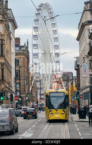 Un tram Bee Network nel mezzo di Manchester City. In lontananza si trova la grande ruota di Albert Square come parte dei mercatini di Natale 2025 Foto Stock