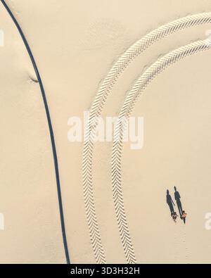 Veduta aerea di due figure che camminano, gettando lunghe ombre sulla sabbia pallida attraversata da piste di pneumatici, Vil nohirs k, Oblast di Dnipropetrovsk, Ucraina. Foto Stock