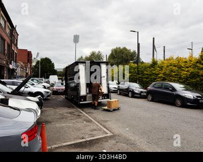 Manchester, Regno Unito - 30 settembre 2025: L'addetto alle consegne scarica una scatola di cartone da un camion nero in una strada di Manchester. Foto Stock
