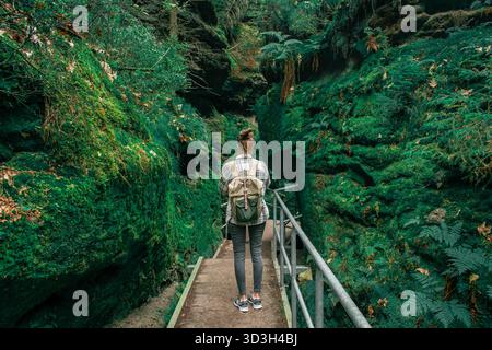 Germania, Sassone. Una ragazza che cammina lungo un sentiero attraverso rocce, completamente ricoperte di muschio, felci e varie piante. Foto Stock