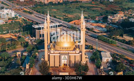 Vista aerea di una moschea con cupola dorata che riflette la luce del sole, giustapposta alle linee architettoniche moderne degli edifici, Abuja, capitale federale Territo Foto Stock