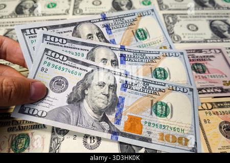 In questa illustrazione fotografica, una mano che tiene in mano diverse nuove banconote da 100 dollari, con varie altre banconote americane sullo sfondo. Foto Stock