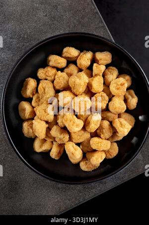 Bocconcini croccanti di popcorn di pollo in una ciotola nera su sfondo grigio. Vista dall'alto. Fast food. Foto Stock