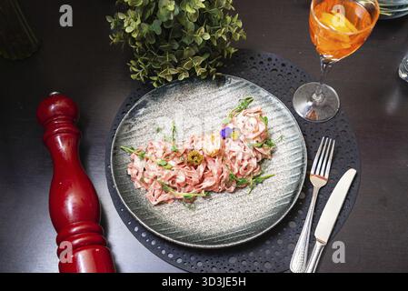 Cibo, vista dall'alto verso il basso della cremosa pasta rosa guarnita con erbe fresche e fiori commestibili, servita con un cocktail su un tavolo nero Foto Stock