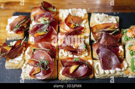 Cibo, eleganti bruschette con fette di pane tostato, condite con panna montata, salumi, erbe e guarnigioni, servite su un vassoio di ardesia Foto Stock