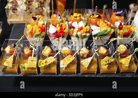 Cibo, Una varietà di antipasti eleganti serviti in bicchieri di plastica trasparente, con verdure, formaggio, frutta e fiori commestibili per eventi Foto Stock