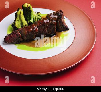Cibo, maiale arrosto con salsa e broccoli su piatto rosso Foto Stock