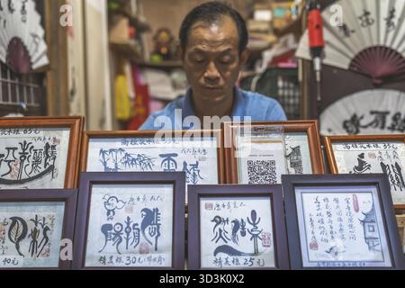 Chongqing, Cina - agosto 2019: Uomo che vende opere d'arte incorniciate nel negozio di caligrafia nella città antica di ci Qi Kou Foto Stock