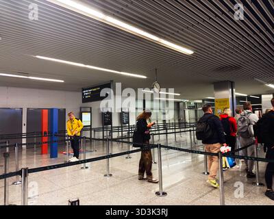 Balice, Polonia - 4 ottobre 2025: I passeggeri fanno la fila all'aeroporto di Cracovia per il check-in mentre un membro del personale si trova nelle vicinanze. Foto Stock