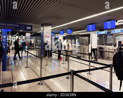Balice, Polonia - 4 ottobre 2025: I viaggiatori sono in fila presso un moderno checkpoint di sicurezza dell'aeroporto di Cracovia con schermi blu. Foto Stock